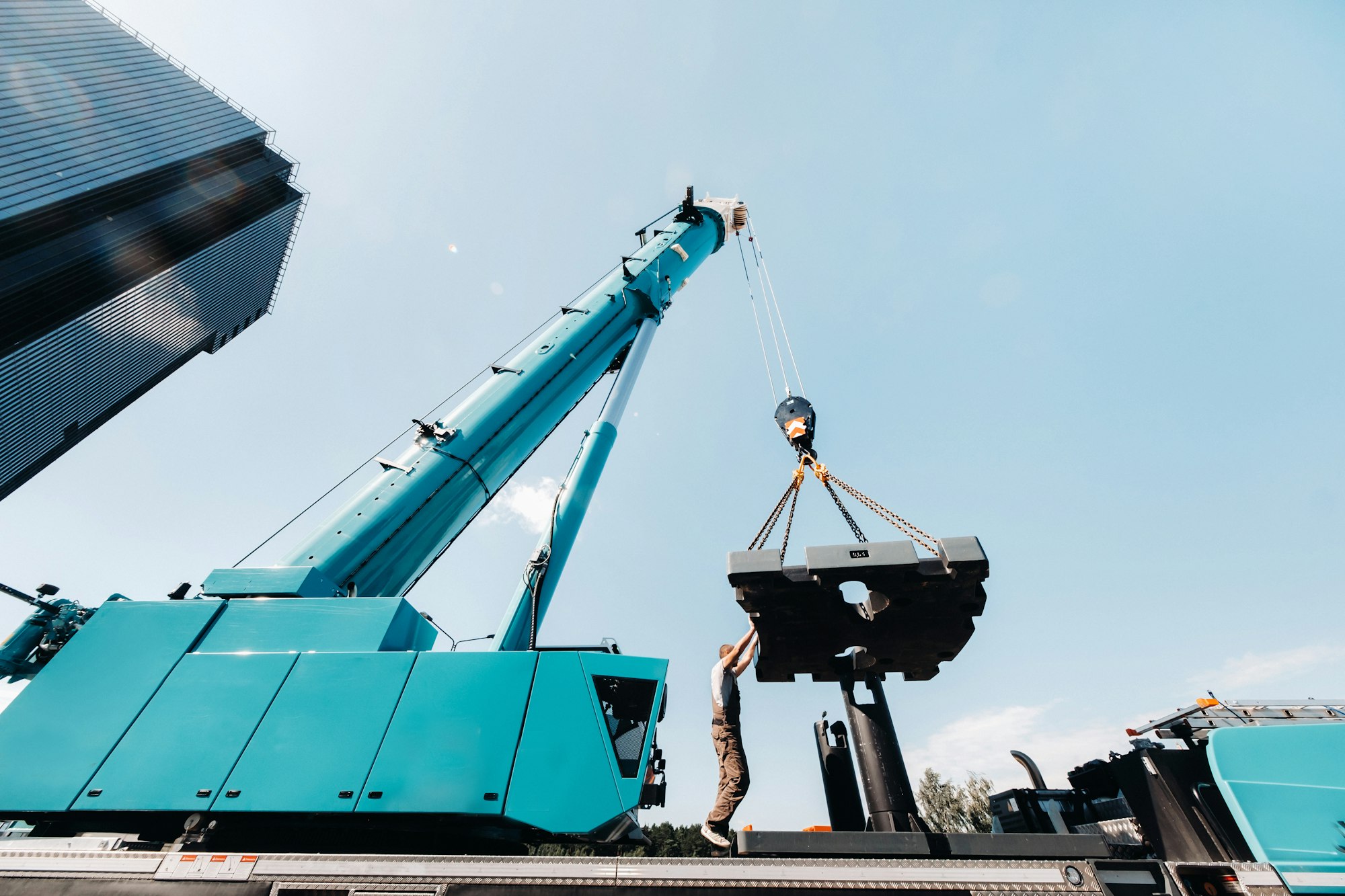 the counterweight is installed by an unrecognizable worker on a large blue car crane and is prepared